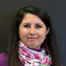 nicoletti bellinger headshot, lady with long dark hair, purple top and pink and white scarf in front of black background