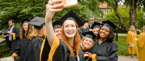 multiple students leaning in for a selfie photo in graduation attire